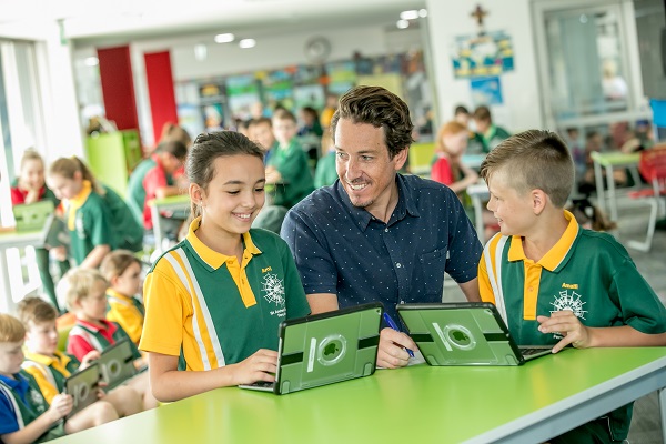 two students sitting in the school library with teacher and looking at iPads